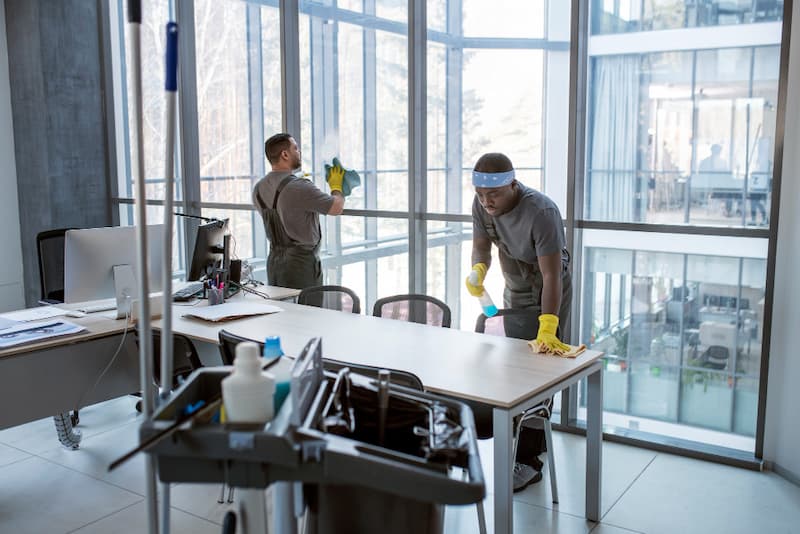 Reinigungsmitarbeiter reinigen ein helles Büro mit großen Fensterfronten